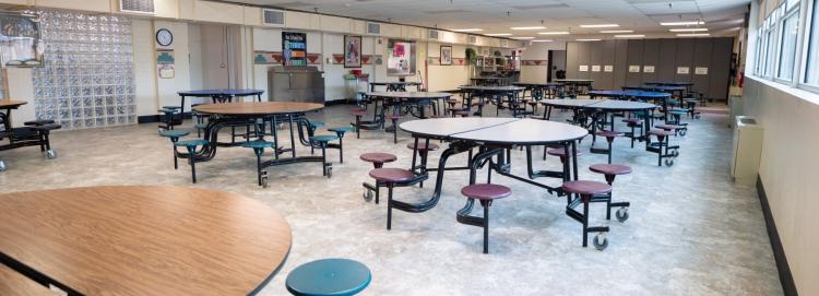A school cafeteria featuring several tables and chairs arranged for students to sit and eat.