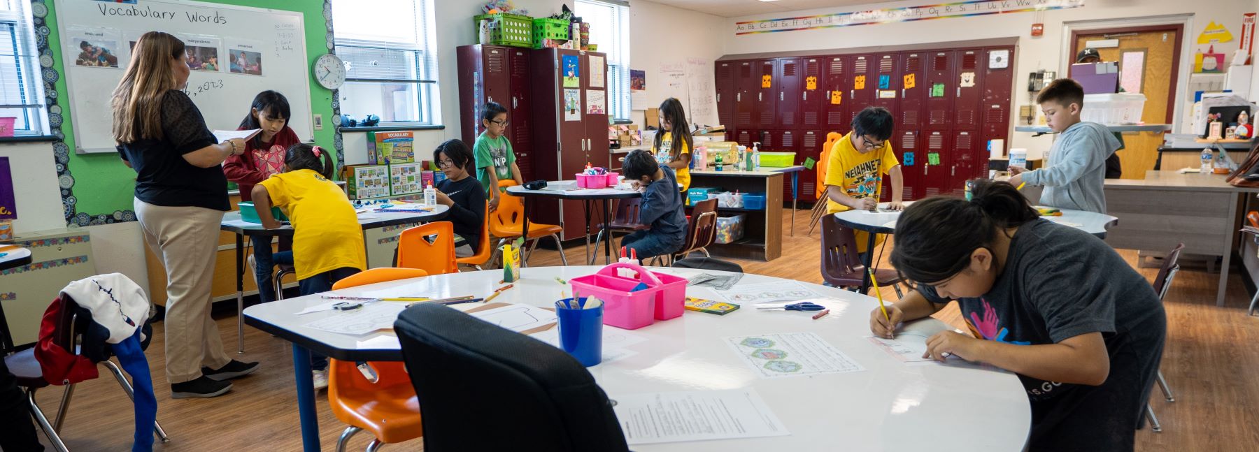 Classroom scene with kids seated at tables, engaged in writing activities.